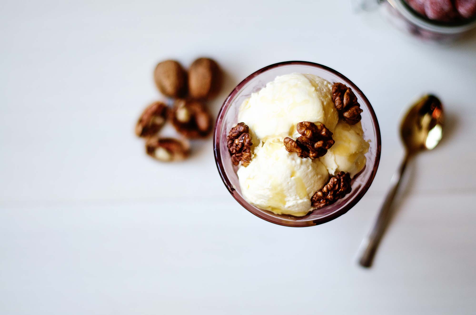 2 scoops of vanilla ice cream in a glass cup, topped with olive oil and walnuts.