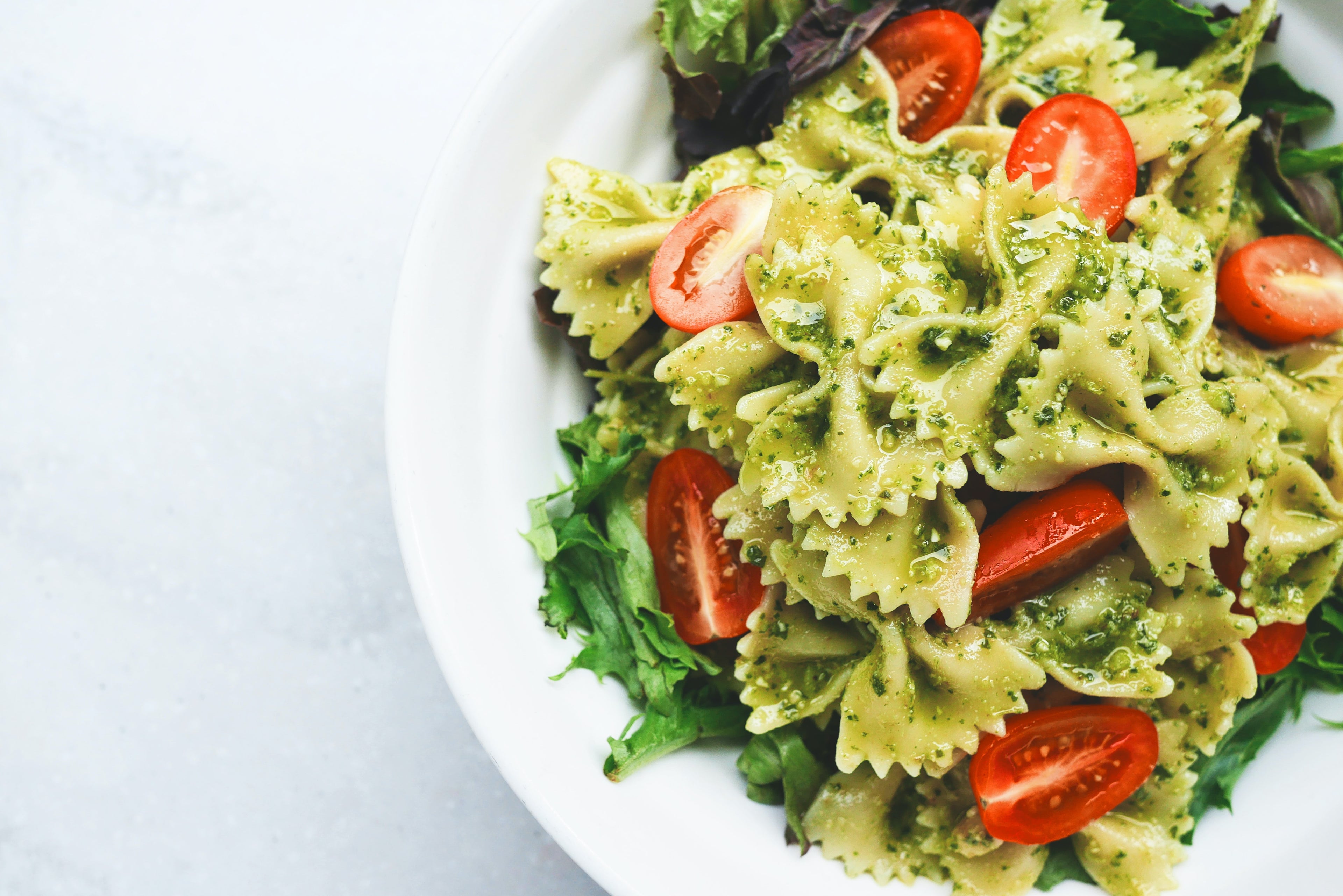 Bowtie pasta with pesto, arugula, and halved cherry tomatoes on a white plate.