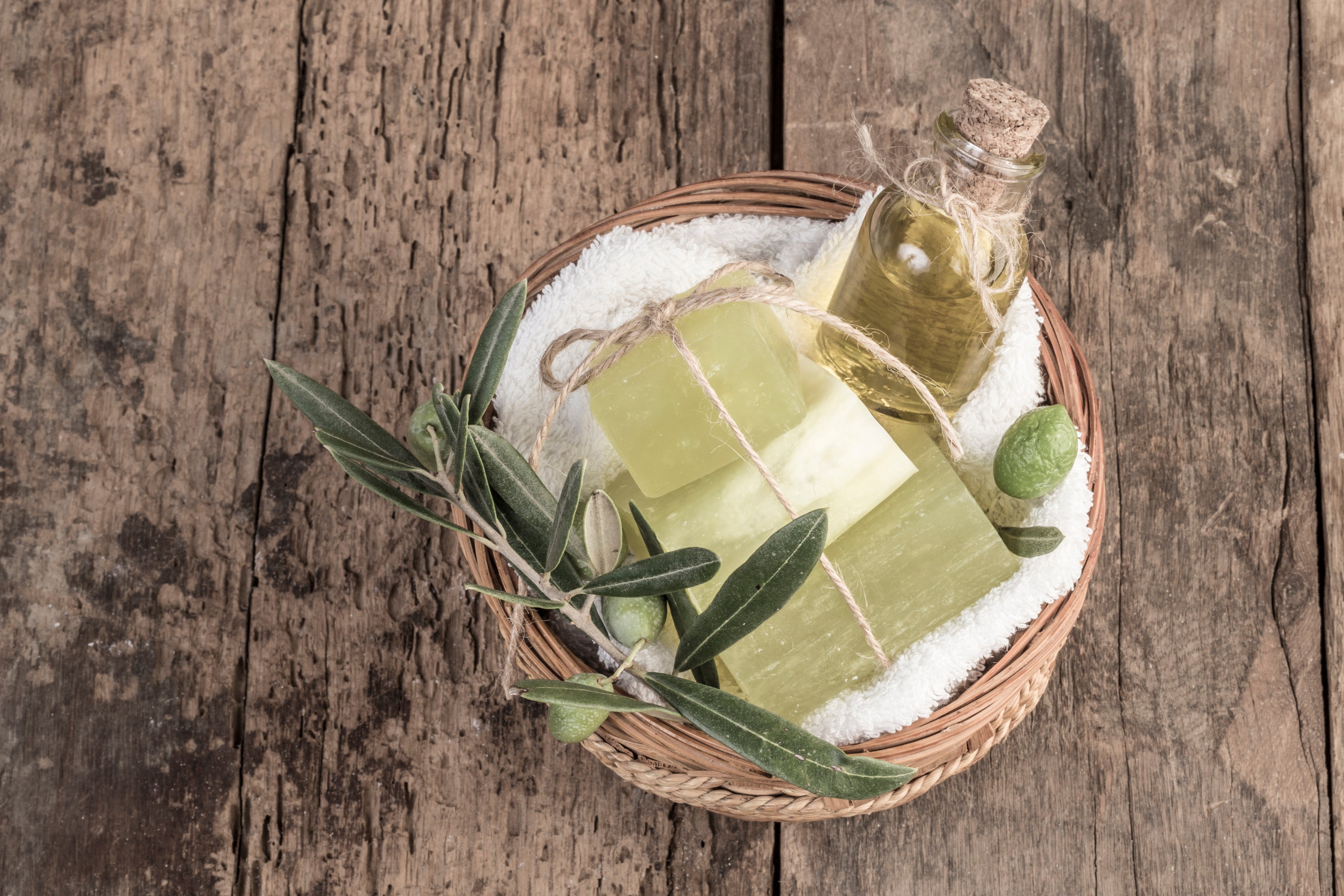 A wicker basket filled with a bottle of olive oil, olive oil soap, and olive leaves.