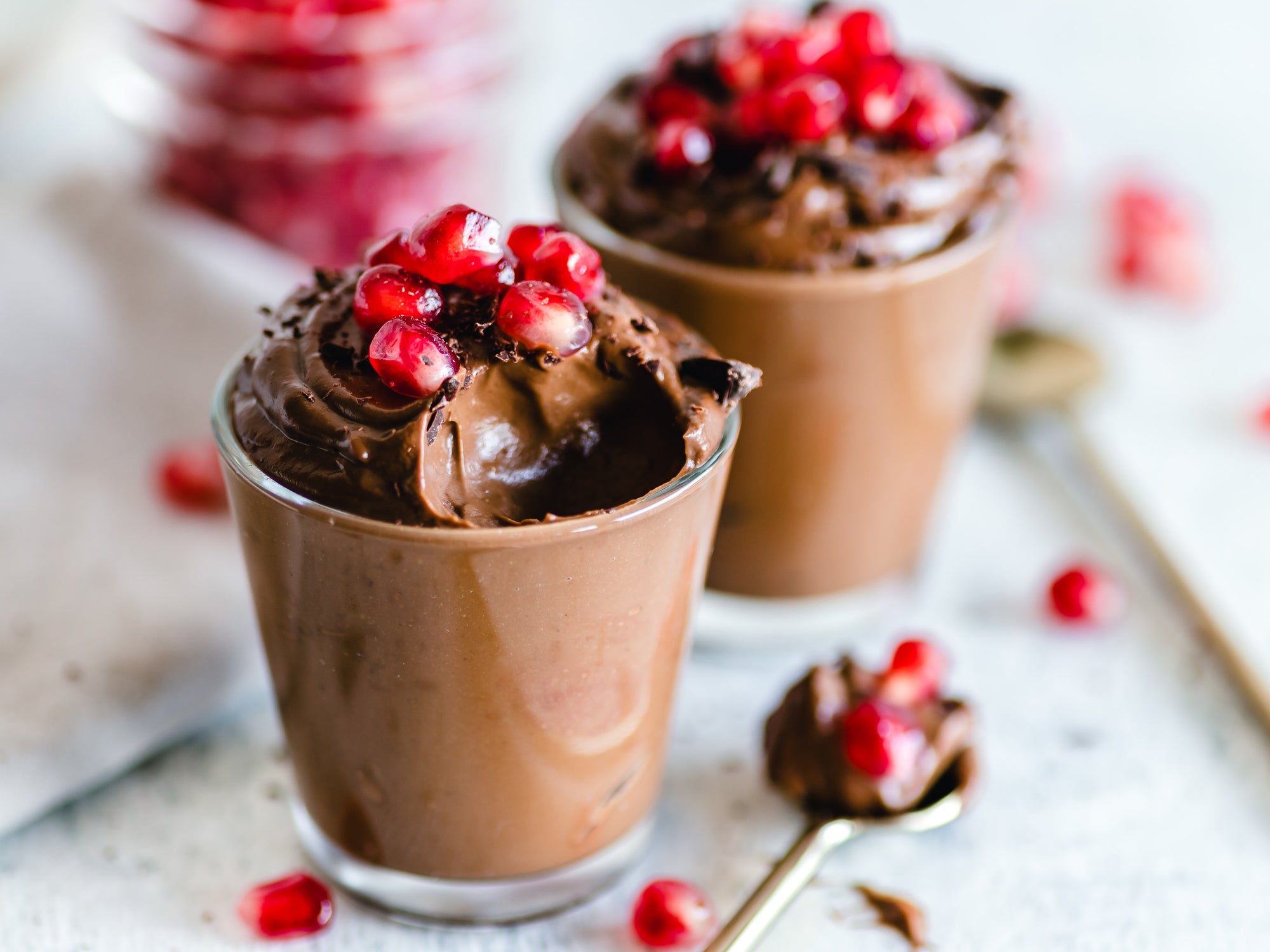 Two cups of chocolate mousse topped with chocolate shavings and pomegranate seeds.